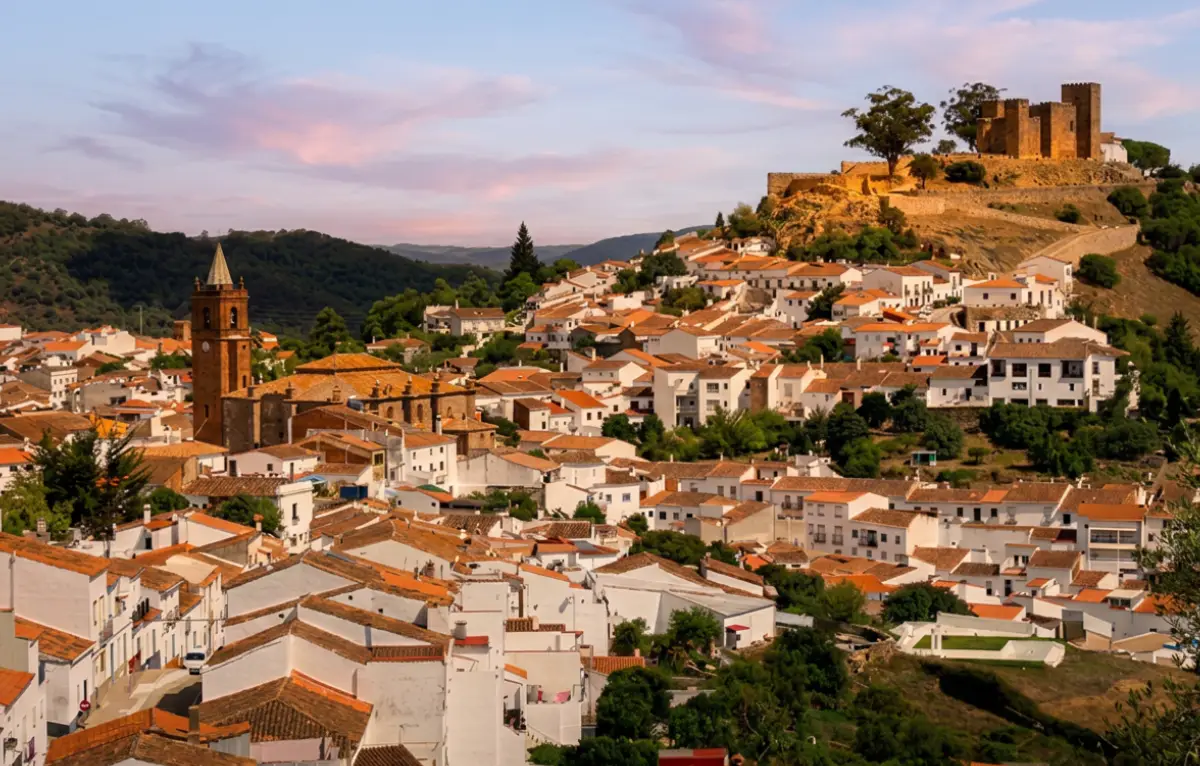 Whitewashed village of Cortegana with its hilltop medieval castle and church bell tower at sunset in the Sierra de Aracena