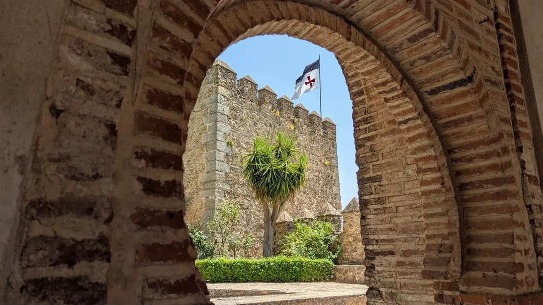 Vistas de la torre del homenaje y bandera templaria desde un arco de ladrillo en la visita privada al Castillo de Cortegana.
