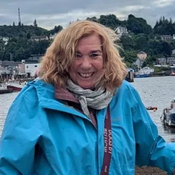 Luz Bona Puerta con pañuelo claro sonriendo frente a un muro de piedra natural durante un tour Innyou