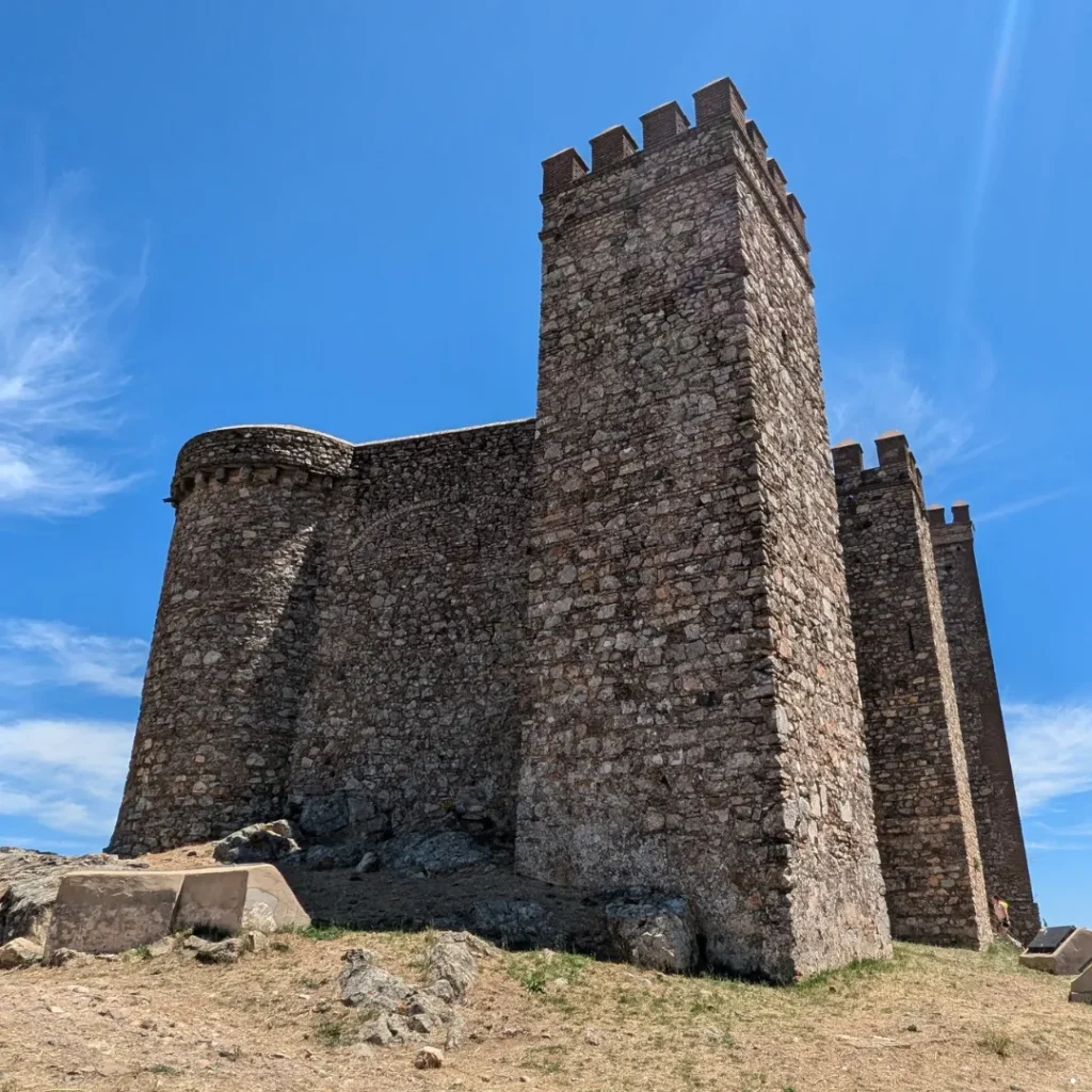 Torres de piedra y murallas medievales bajo un cielo despejado durante una visita privada al Castillo de Cortegana.